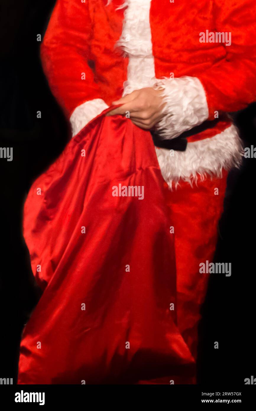 Les mains du Père Noël dans un costume de Père Noël du nouvel an grimpent dans un sac rouge avec des cadeaux gros plan sur un fond sombre. Banque D'Images