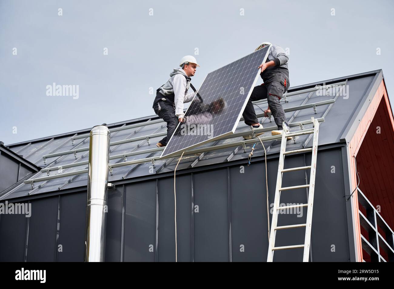 Installateurs installant le système de panneau solaire sur le toit de la maison. Hommes travailleurs dans des casques portant le module solaire photovoltaïque à l'extérieur. Concept d'énergie alternative et renouvelable. Banque D'Images