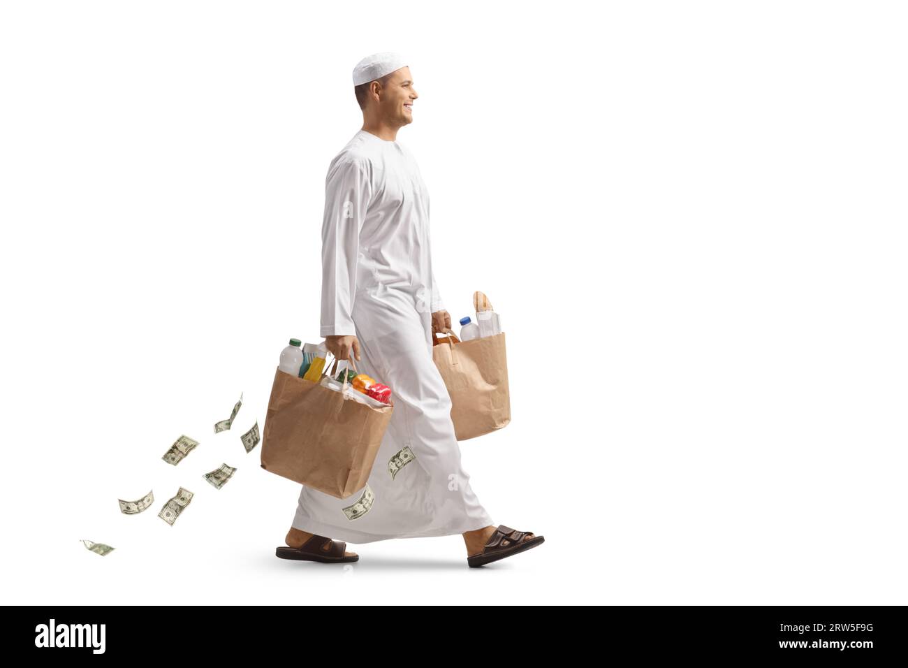 Homme arabe en vêtements ethniques marchant et portant des sacs d'épicerie et de l'argent tombant derrière isolé sur fond blanc Banque D'Images