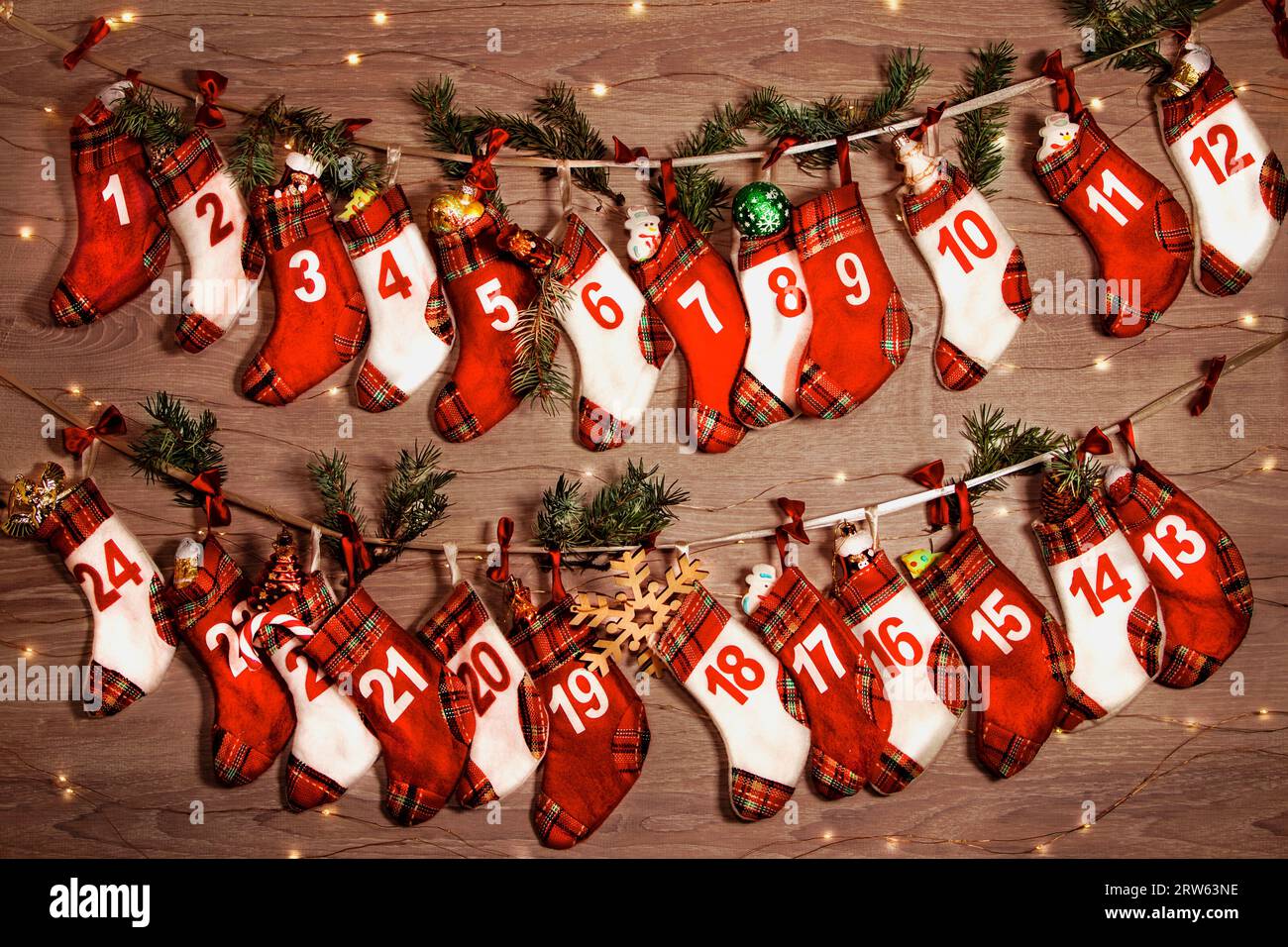 Calendrier de l'Avent avec des cadeaux dans les chaussettes des enfants. Branches d'un arbre de Noël, lumières de guirlandes sur un fond en bois. 24 chaussettes de l'Avent ca Banque D'Images