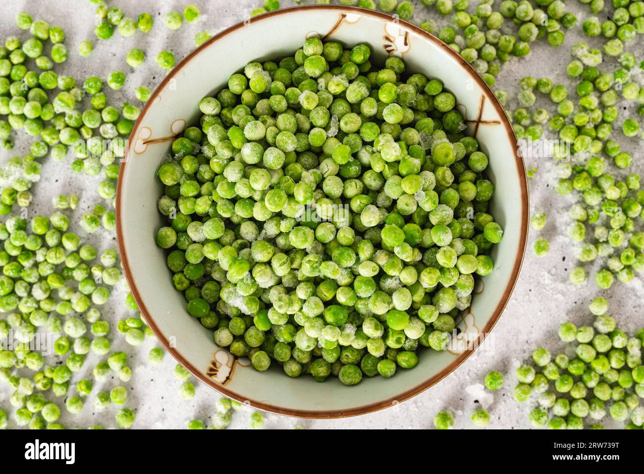 Pois verts congelés dans un bol en gros plan d'en haut sur fond gris clair Banque D'Images