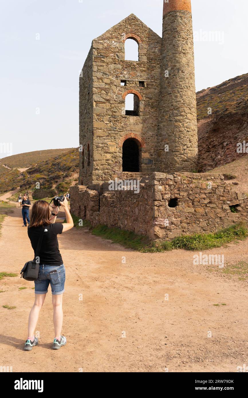 Touriste photographiant les ruines historiques de la maison de moteur de la mine d'étain de Cornish avec cheminée en pierre Banque D'Images