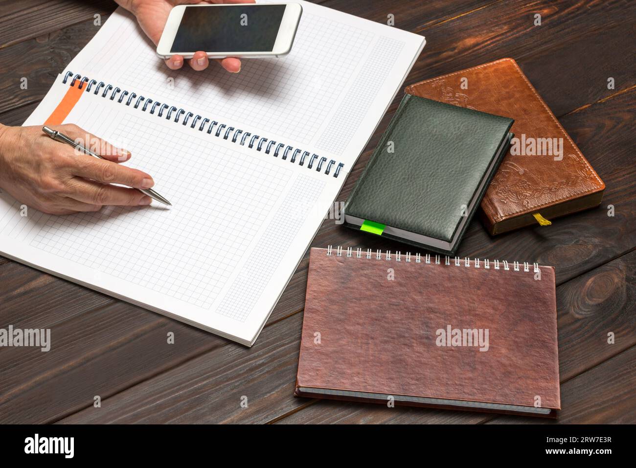 Mains tiennent le stylo et le smartphone, ordinateur portable ouvert. Sur la calculatrice de table et les cahiers. Vue de dessus. Fond en bois foncé Banque D'Images