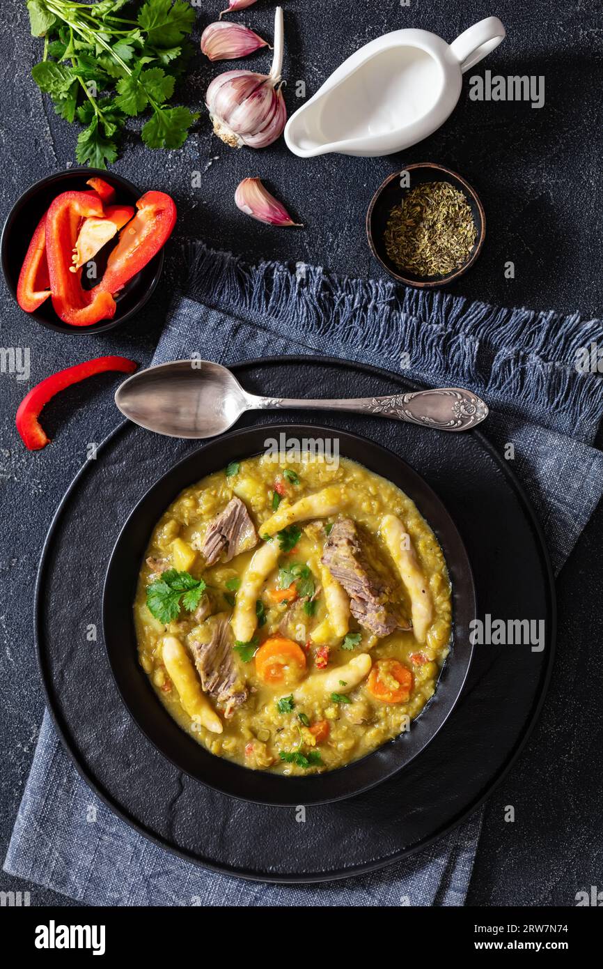 pois gungo, soupe de pois pigeons avec boulettes et bœuf dans un bol noir sur une table en béton avec des ingrédients, cuisine jamaïcaine, vue verticale d'en haut Banque D'Images
