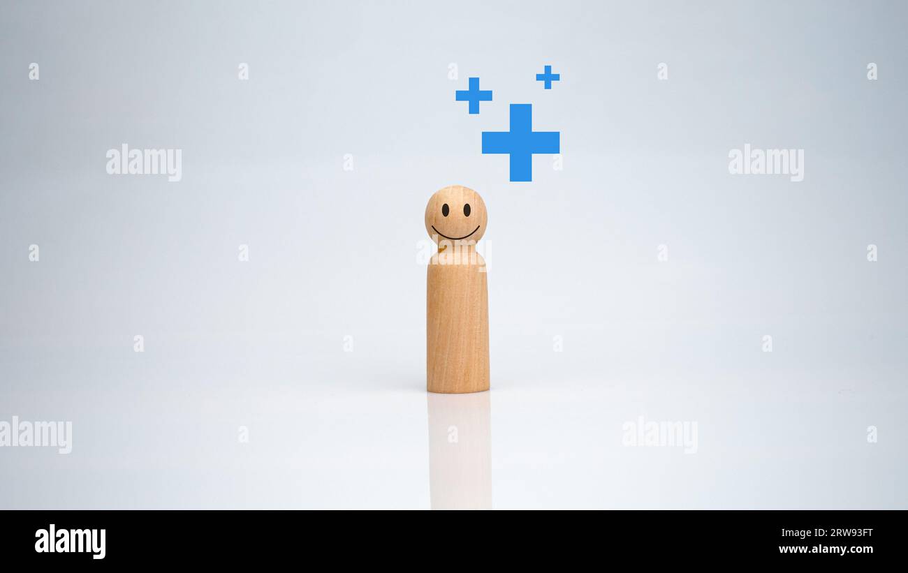 Le concept d'assurance maladie et de bien-être médical. Une poupée en bois avec un signe plus sur un fond blanc représente la protection, recevant des avantages. h Banque D'Images