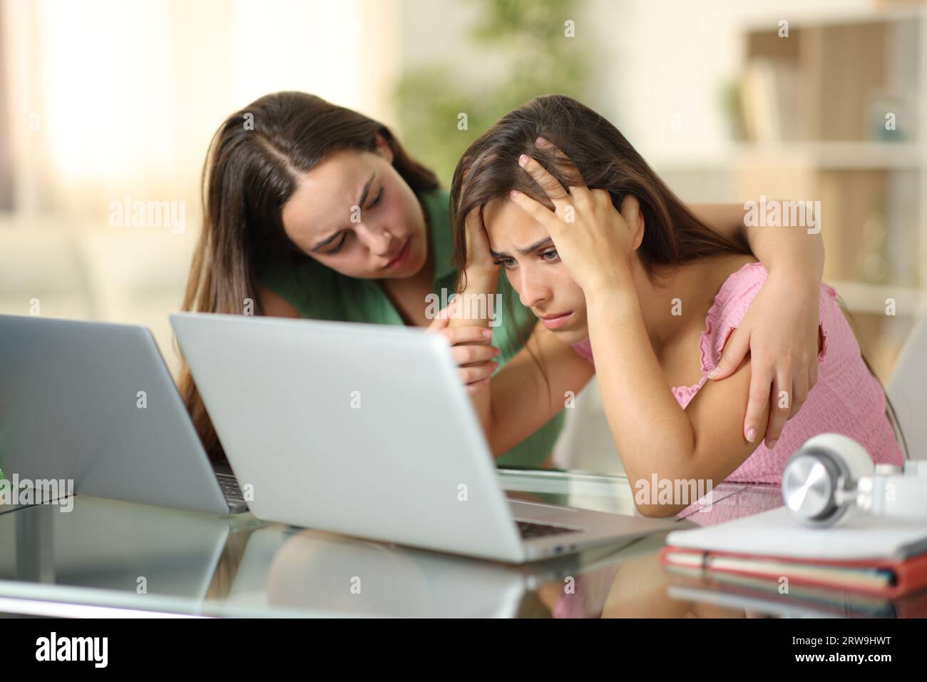 Triste étudiant étant réconforté par un autre vérifiant son ordinateur portable à la maison Banque D'Images