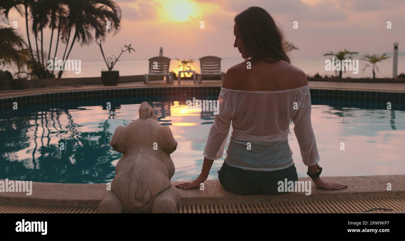 Femme assis près de la piscine, profiter de la vue spectaculaire coucher de soleil sur l'horizon de l'océan. Palmiers et transats, Resort tropical de luxe en Thaïlande, île de Koh Phangan. Voyage, tourisme, vacances d'été, paysage de la nature Banque D'Images