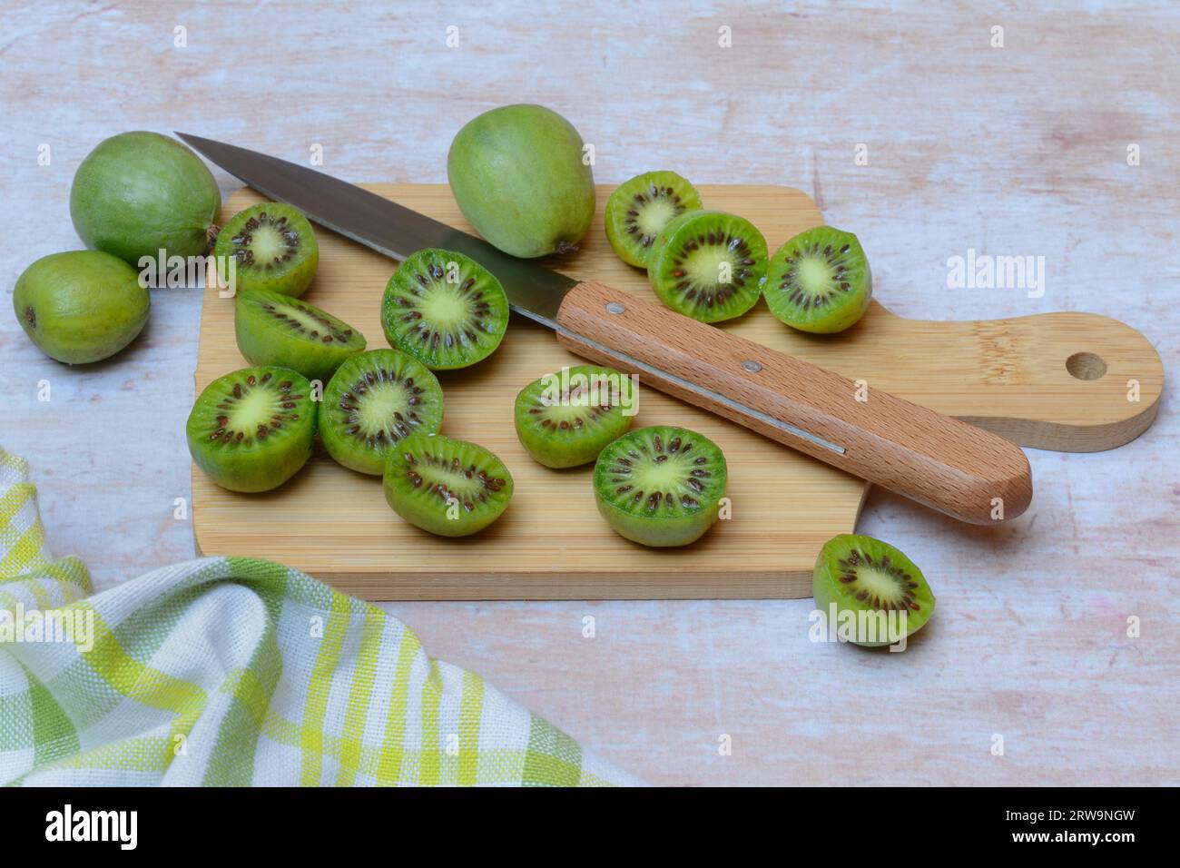 Mini kiwi, fruits entiers et coupés en deux sur planche de bois avec couteau (Actinidia arguta) Banque D'Images