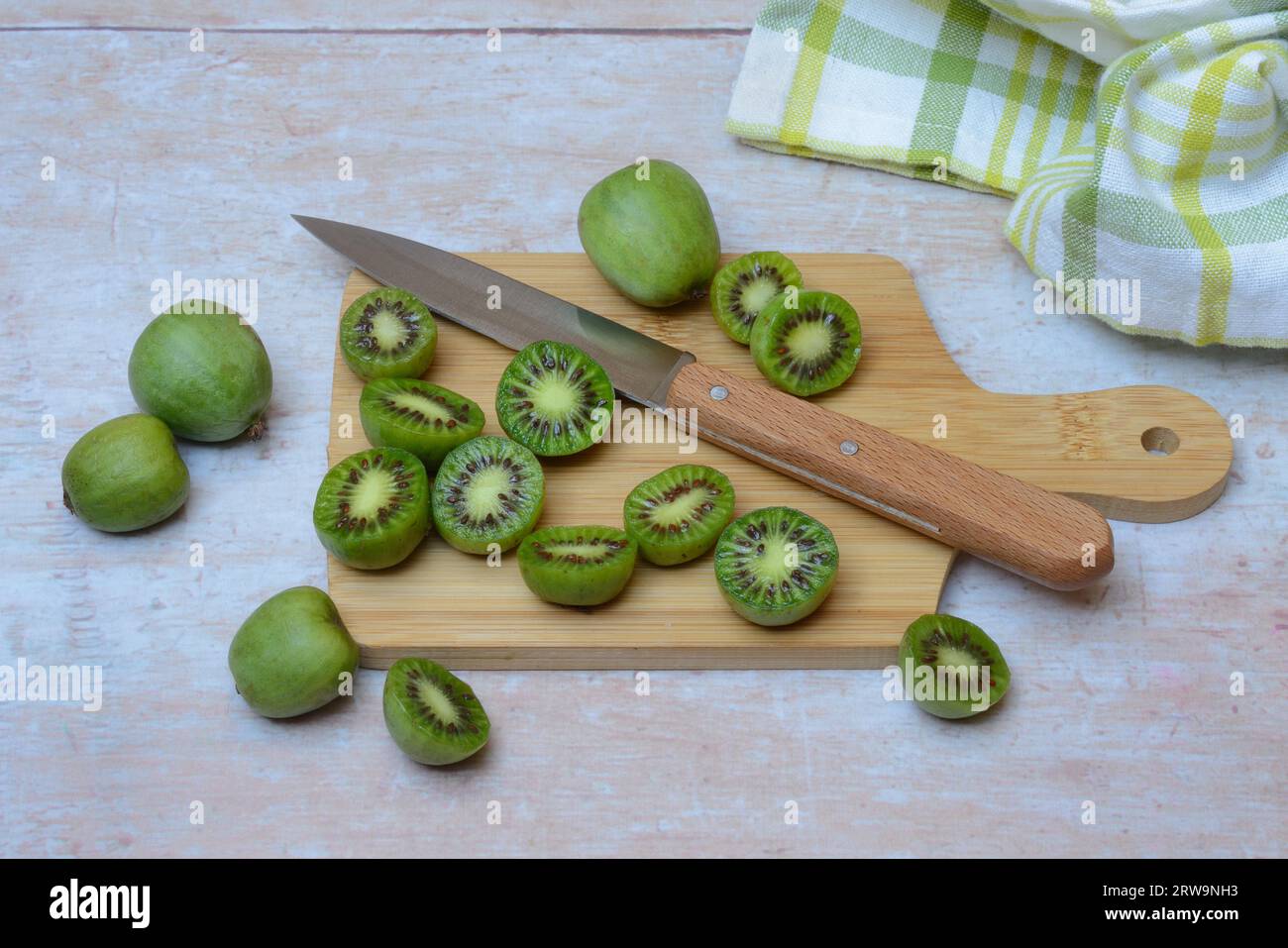 Mini kiwi, fruits entiers et coupés en deux sur planche de bois avec couteau (Actinidia arguta) Banque D'Images