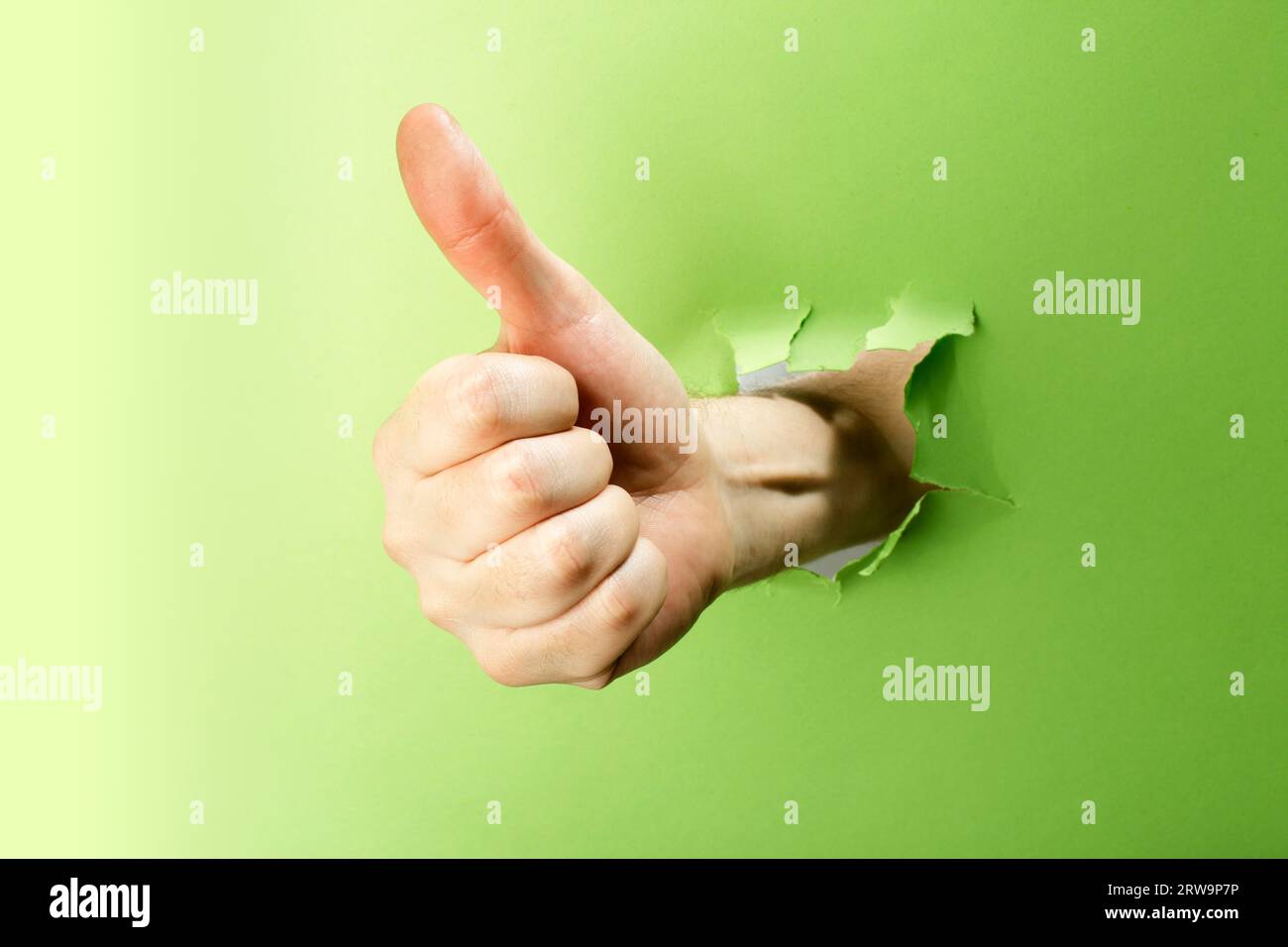Homme faisant le geste de pouce vers le haut à travers le papier vert Banque D'Images