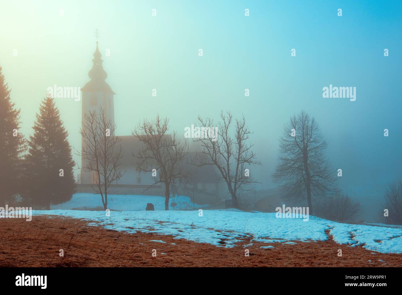 Église de St. Jean le Baptiste par le lac Bohinj à Ribcev Laz, Slovénie dans le matin brumeux. Exemple vieux de 700 ans de l'architecture médiévale slovène. Banque D'Images