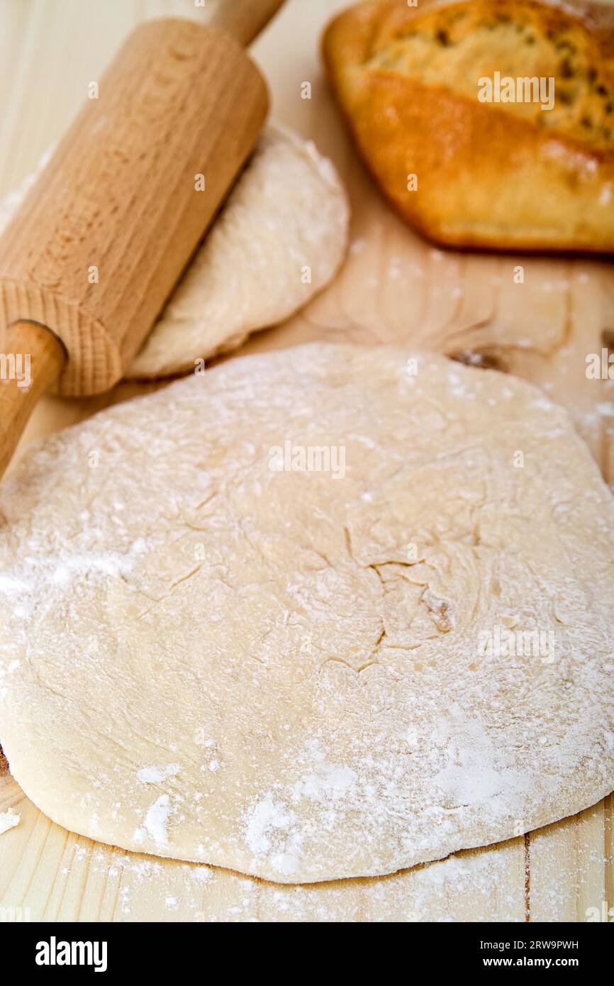 Étaler la pâte à levures sur une planche de bois. Derrière elle un rouleau de pâte et un petit pain Banque D'Images