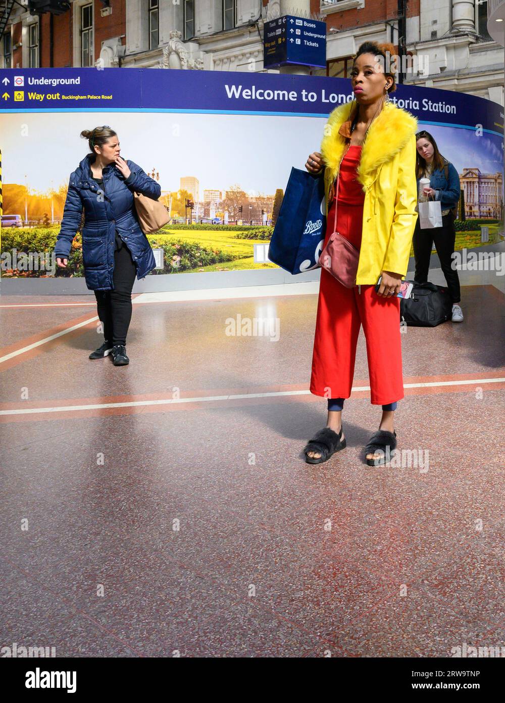 Londres, Royaume-Uni. Femme vêtue de couleurs vives sur le hall de Victoria Station Banque D'Images