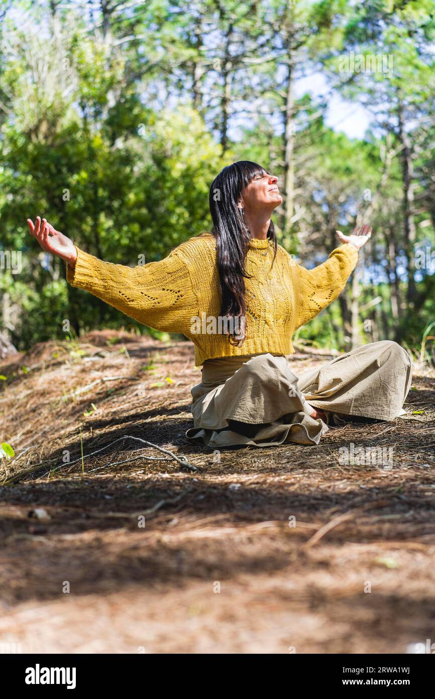 Femme assise sur les bois avec les bras ouverts tout en regardant vers le ciel comme remerciant Dieu. Tir vertical Banque D'Images