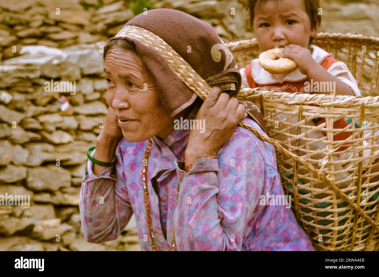 Beni, Népal, vers mai 2012 : une femme indigène avec un couvre-chef porte un panier sur son dos avec son enfant dedans qui mange du gâteau et elle monte la colline à Beni Banque D'Images