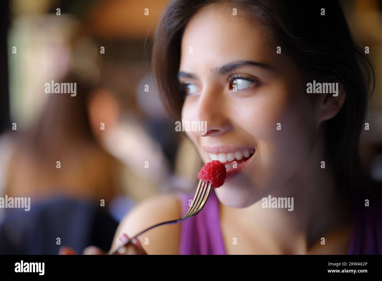 Femme heureuse mangeant blackberry regardant le côté assis dans un restaurant Banque D'Images