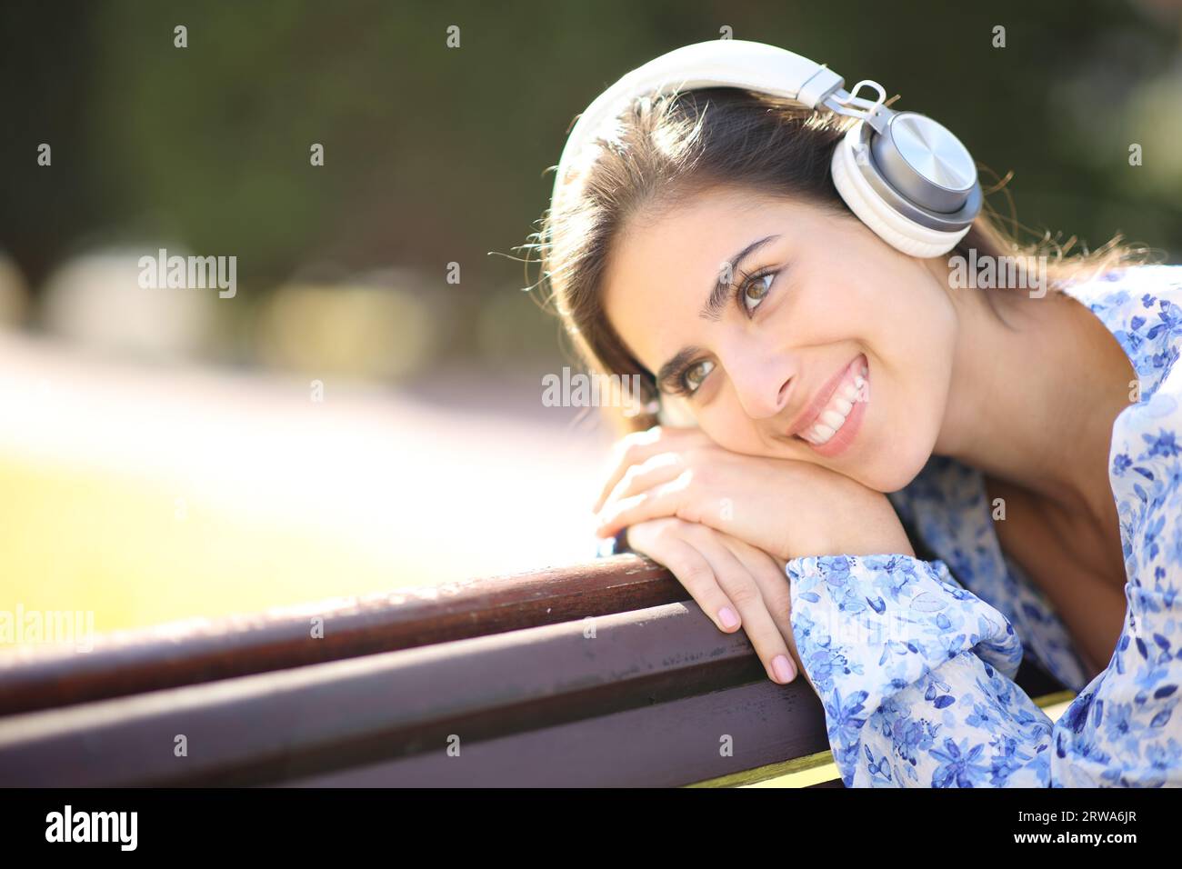 Femme heureuse wering casque appréciant l'audio sur un banc dans un parc Banque D'Images