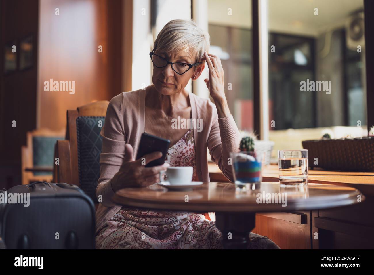 Femme mature est assise dans un café à l'aéroport, attendant l'embarquement. Elle examine l'horaire sur smartphone. Banque D'Images