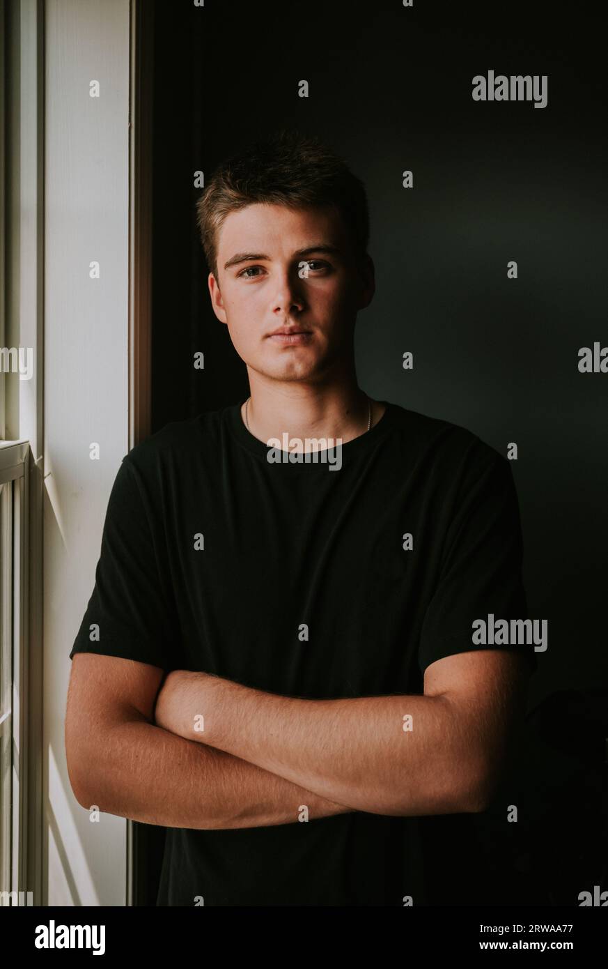 Portrait de beau garçon adolescent debout à côté de la fenêtre dans la chambre sombre. Banque D'Images