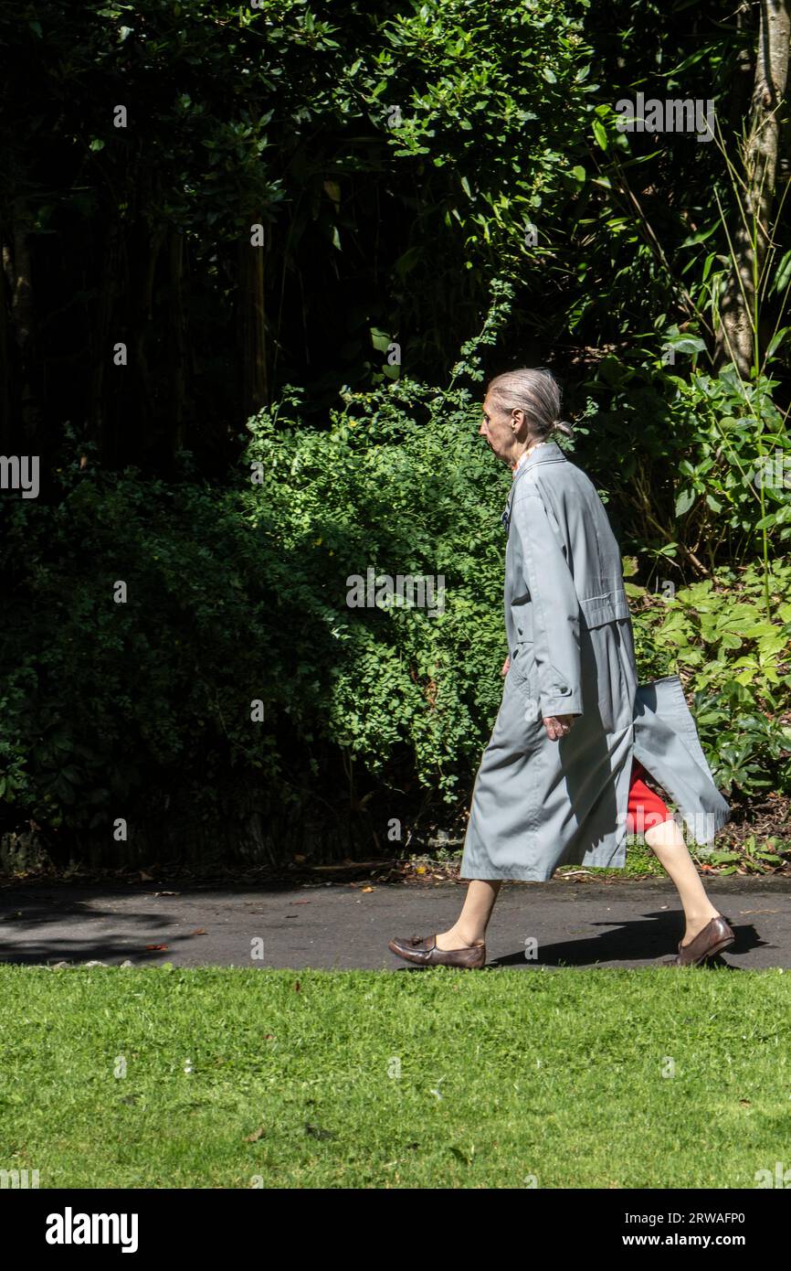 Une dame mature portant un pardessus marchant au soleil à Newquay en Cornouailles au Royaume-Uni Banque D'Images