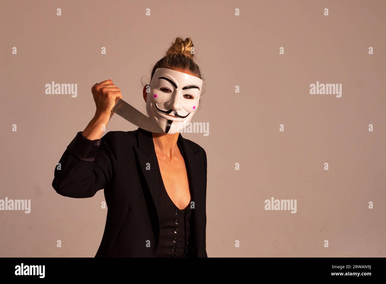 Femme avec un masque anonyme vêtue d'une veste de costume de couleur noire, portant un couteau dans sa main, préparée pour la fête d'Halloween Banque D'Images