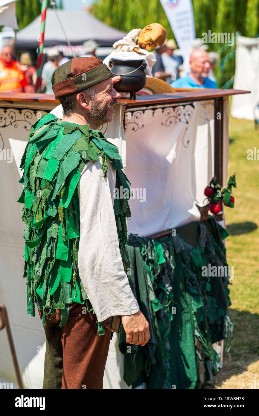 Marionnettiste médiéval dans un costume d'époque verte, se produisant avec une marionnette lors d'un événement de reconstitution à Sandwich Town dans le kent en été. Banque D'Images