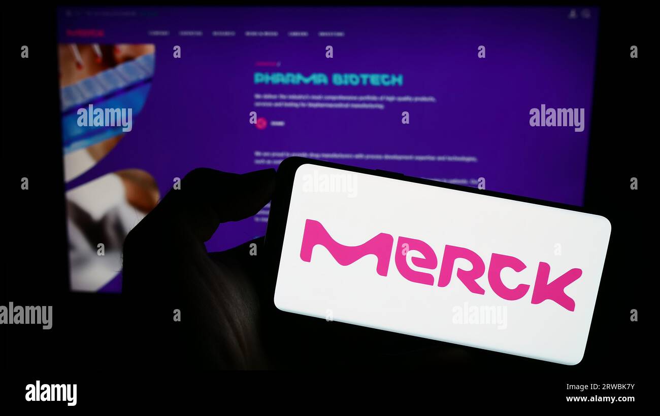 Personne tenant le téléphone portable avec le logo de la société pharmaceutique allemande Merck KGaA sur l'écran en face de la page Web de l'entreprise. Concentrez-vous sur l'affichage du téléphone. Banque D'Images