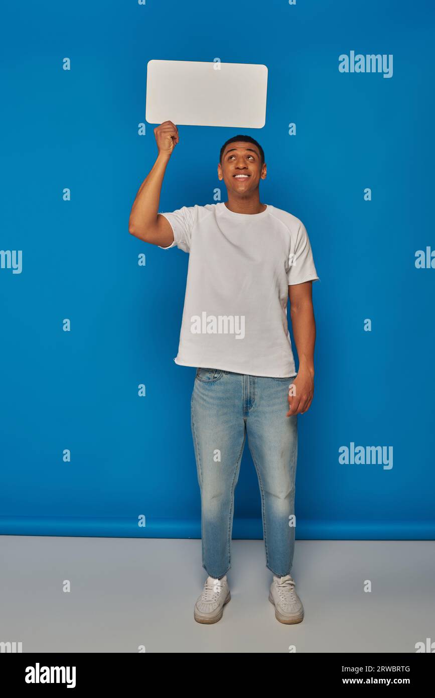 heureux homme afro-américain en jeans denim tenant la bulle de discours sur fond bleu, pleine longueur Banque D'Images