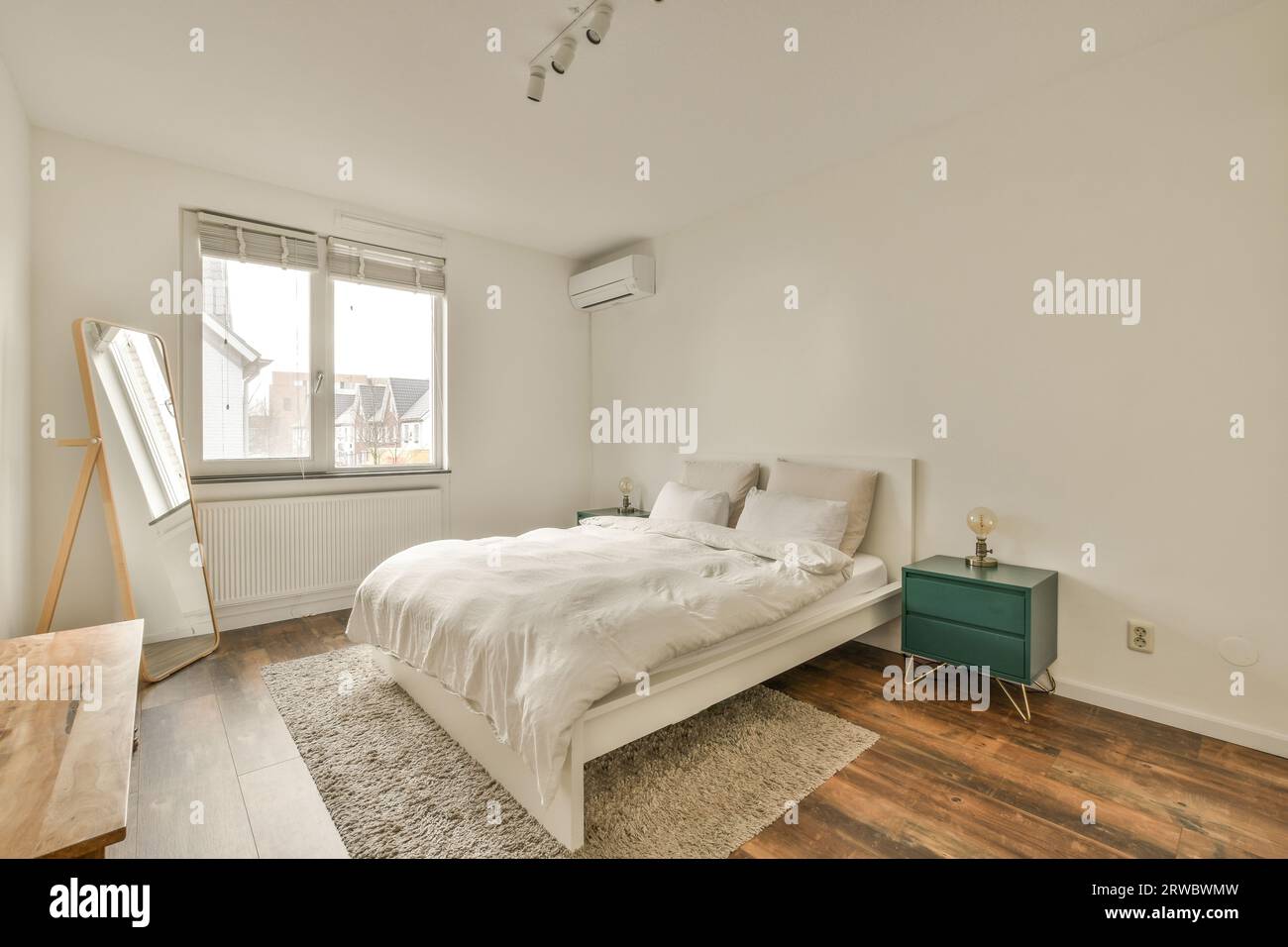 Intérieur de la chambre blanche moderne avec lit confortable et grand miroir à côté de la fenêtre lumineuse dans la maison contemporaine Banque D'Images