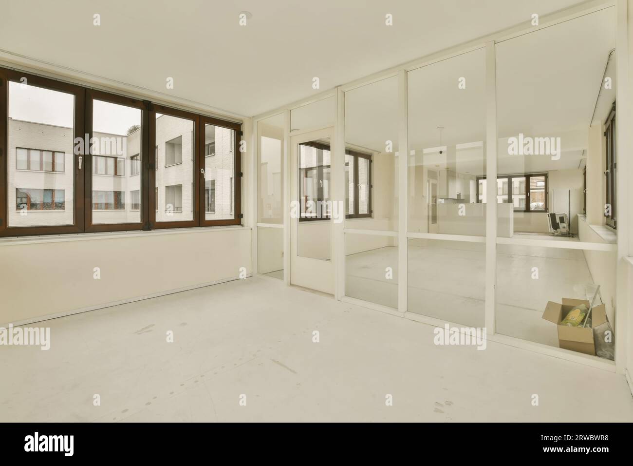 Intérieur de spacieux appartement rénové avec de grandes fenêtres et des murs de verre entre des pièces vides avec des murs blancs et le sol Banque D'Images