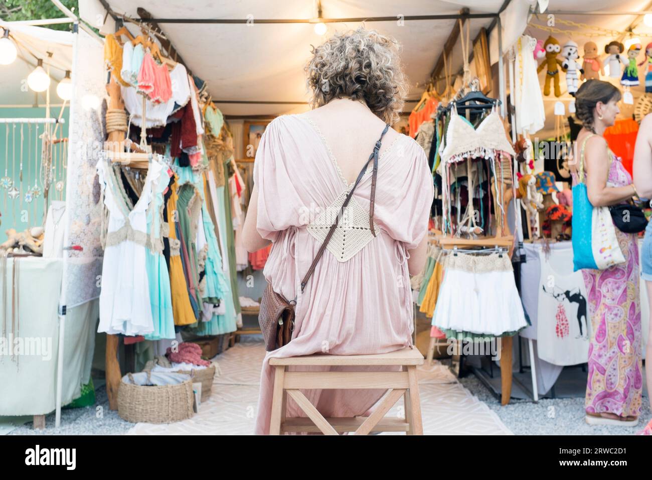 Une femme est assise devant un stand de vêtements au marché hippy Las Dalias à Ibiza, Îles Baléares, Espagne. Banque D'Images