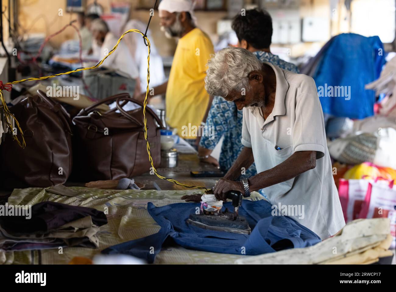 KOCHI, INDE - 28 JANVIER 2023 : un homme repasse manuellement le linge à la laverie locale. Banque D'Images