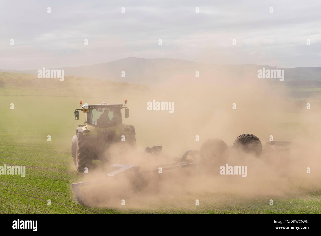 Nuages de poussière par temps sec d'un tracteur avec rouleaux Dal-Bo tournant dans un champ tout en roulant une récolte d'orge de printemps Banque D'Images