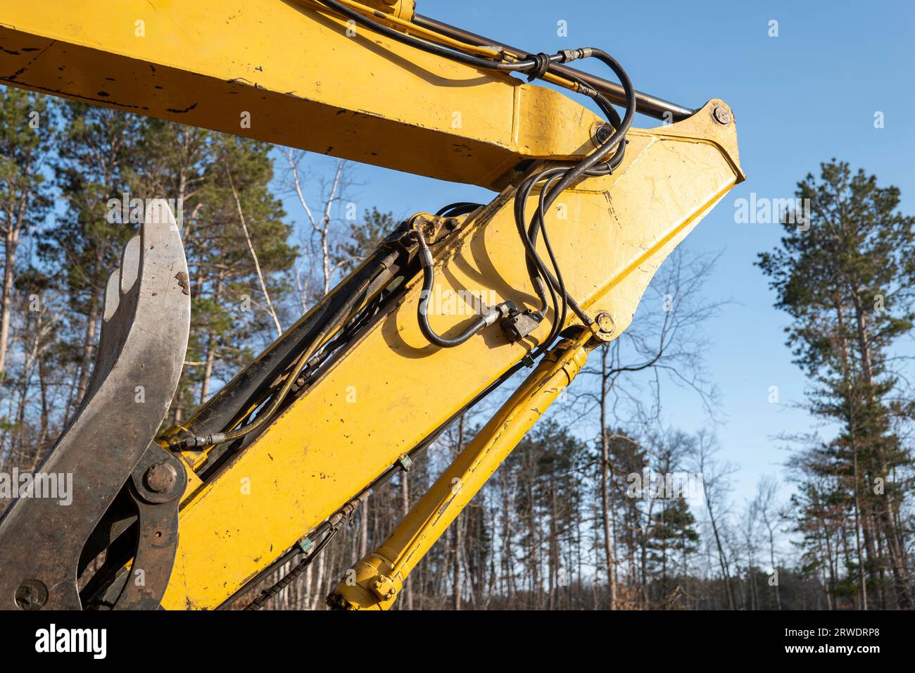 Le coude du bras de flèche et les tubes hydrauliques sur une pelle hydraulique de travail pour équipement lourd sur un nouveau chantier de construction, avec un ciel bleu et des arbres dans le dos Banque D'Images