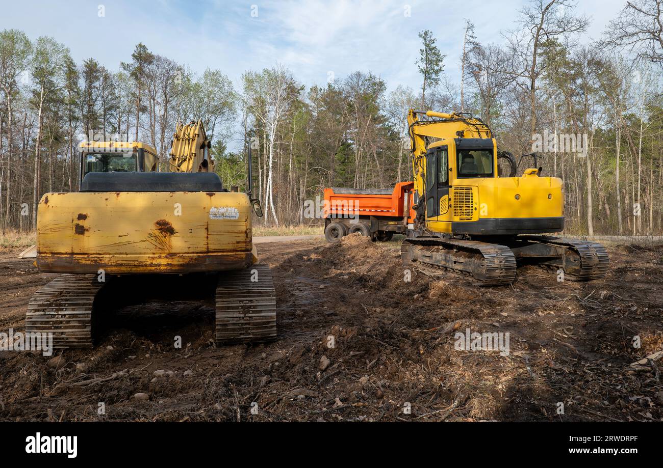 Deux pelles hydrauliques vues de derrière et un camion à benne basculante orange, sur un nouveau chantier de construction de maisons. Banque D'Images