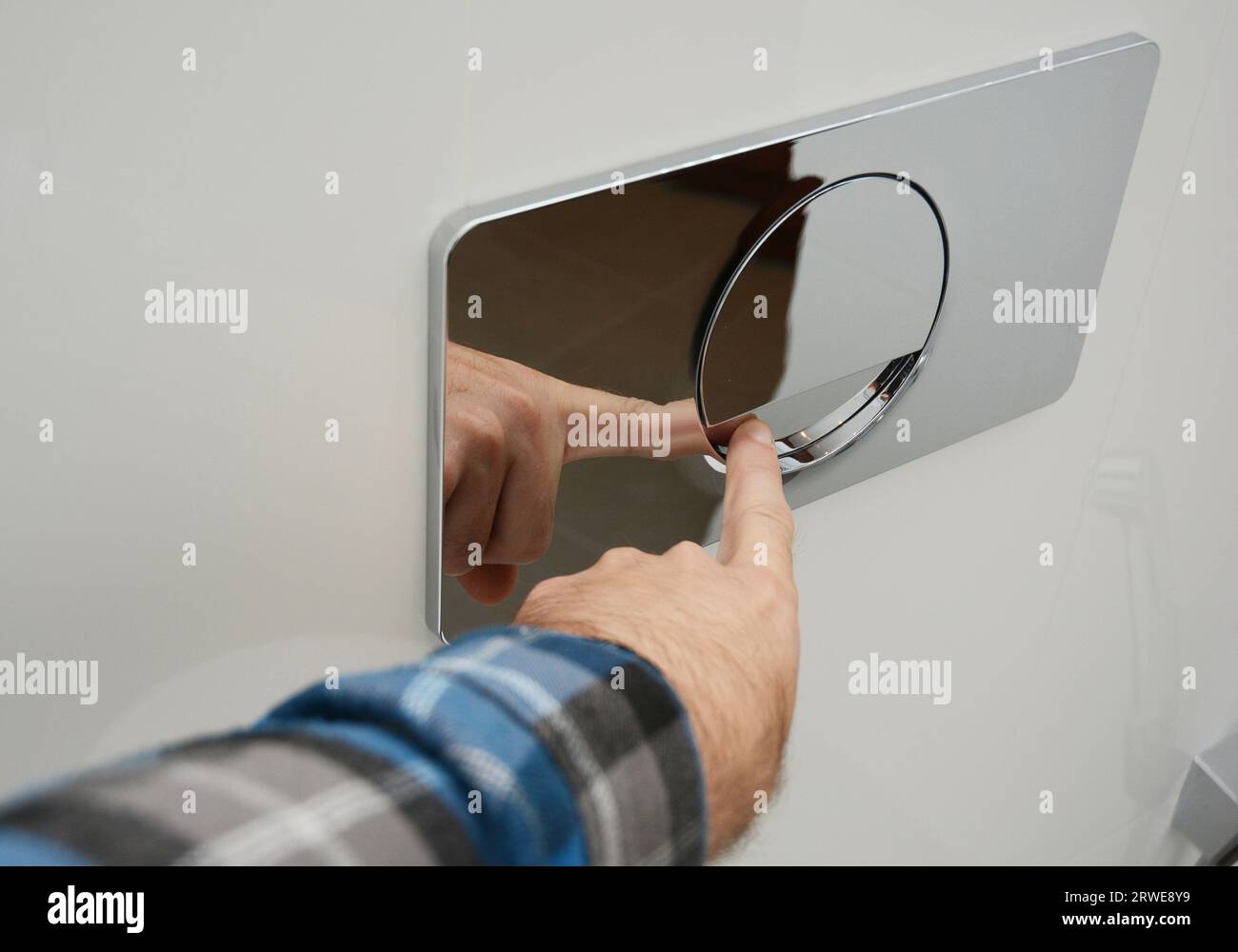 Un homme appuie sur une plaque de rinçage simple en chrome poli fixée au mur pour rincer les toilettes. Banque D'Images