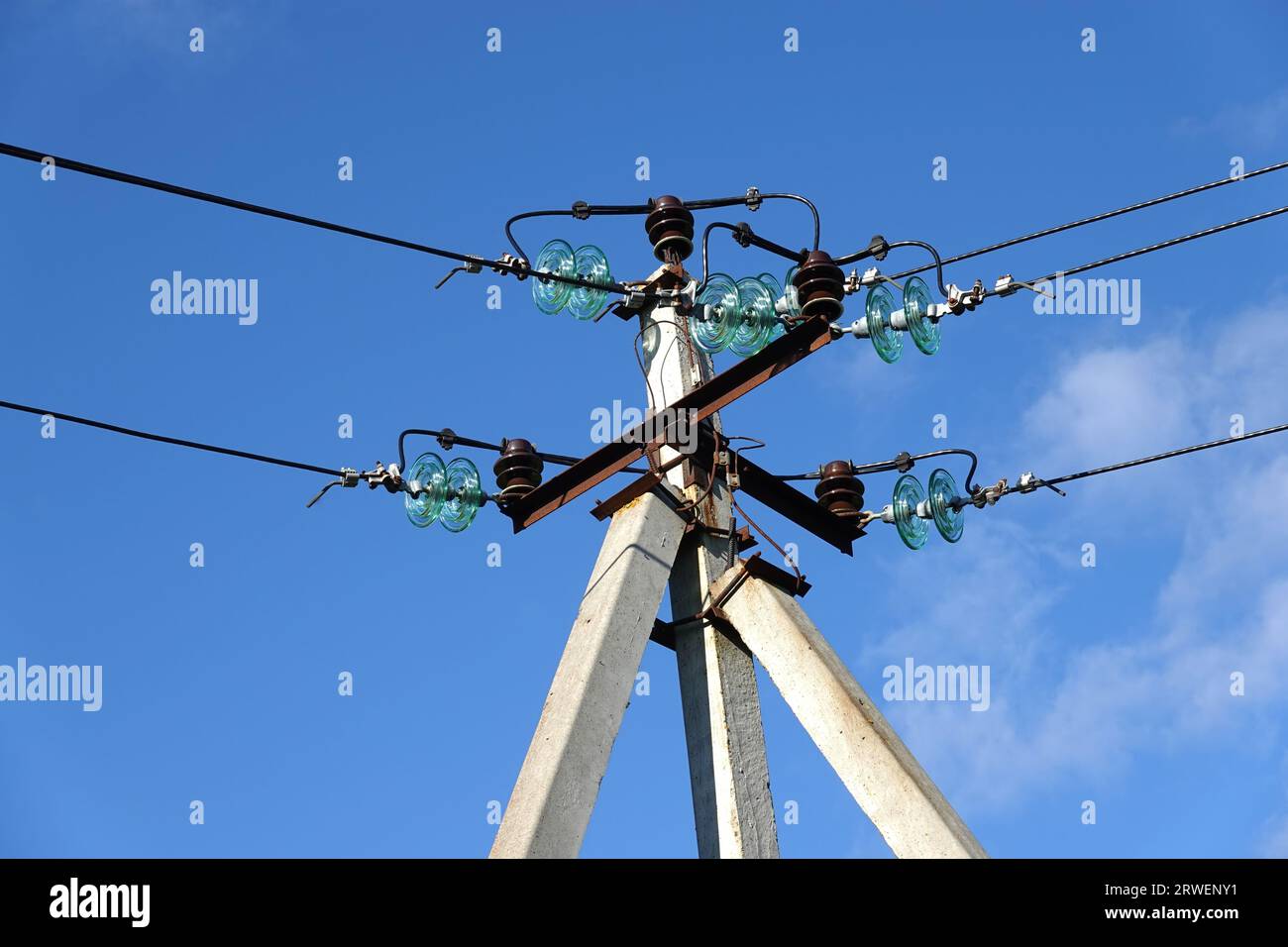 Partie supérieure du pilier de la ligne d'alimentation électrique avec fils et isolants sous ciel bleu avec nuages blancs Banque D'Images