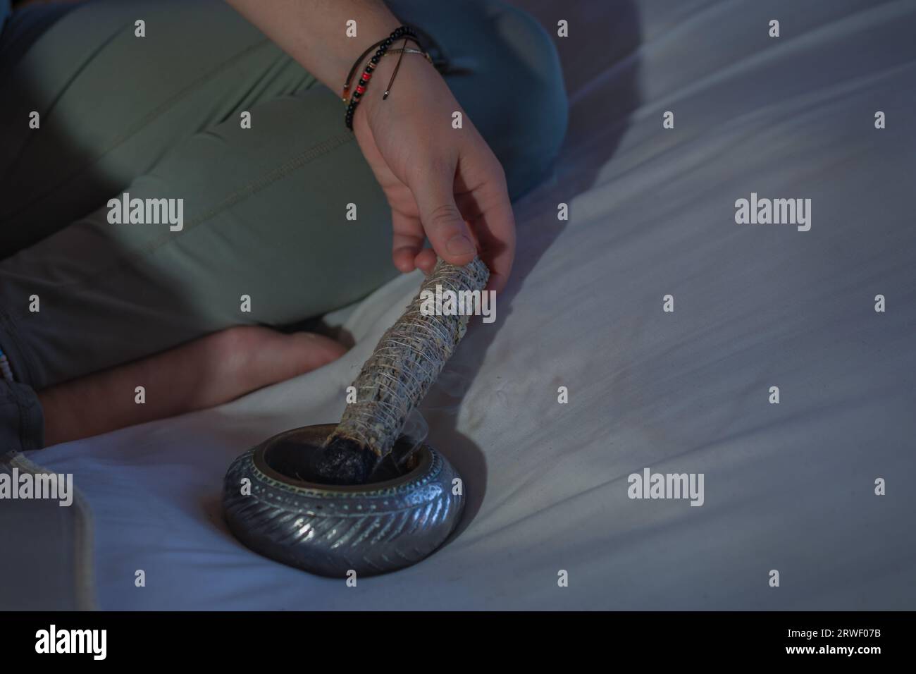 Portrait rapproché d'une main de jeune femme tenant un bâton de fumage sur un bol d'argent pendant la méditation Banque D'Images