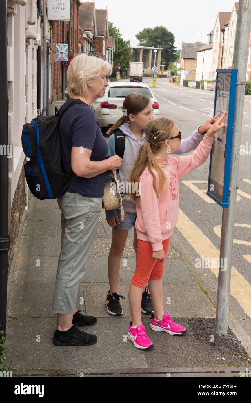 jeunes filles avec grand-mère debout à un arrêt de bus essayant de travailler sur l'horaire ou l'horaire, les transports publics Banque D'Images