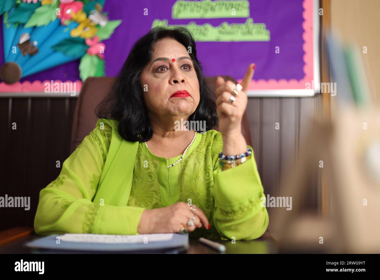 Directrice d'école assise dans son bureau avec agressivité, fuyant avec colère, expression furieuse. Banque D'Images