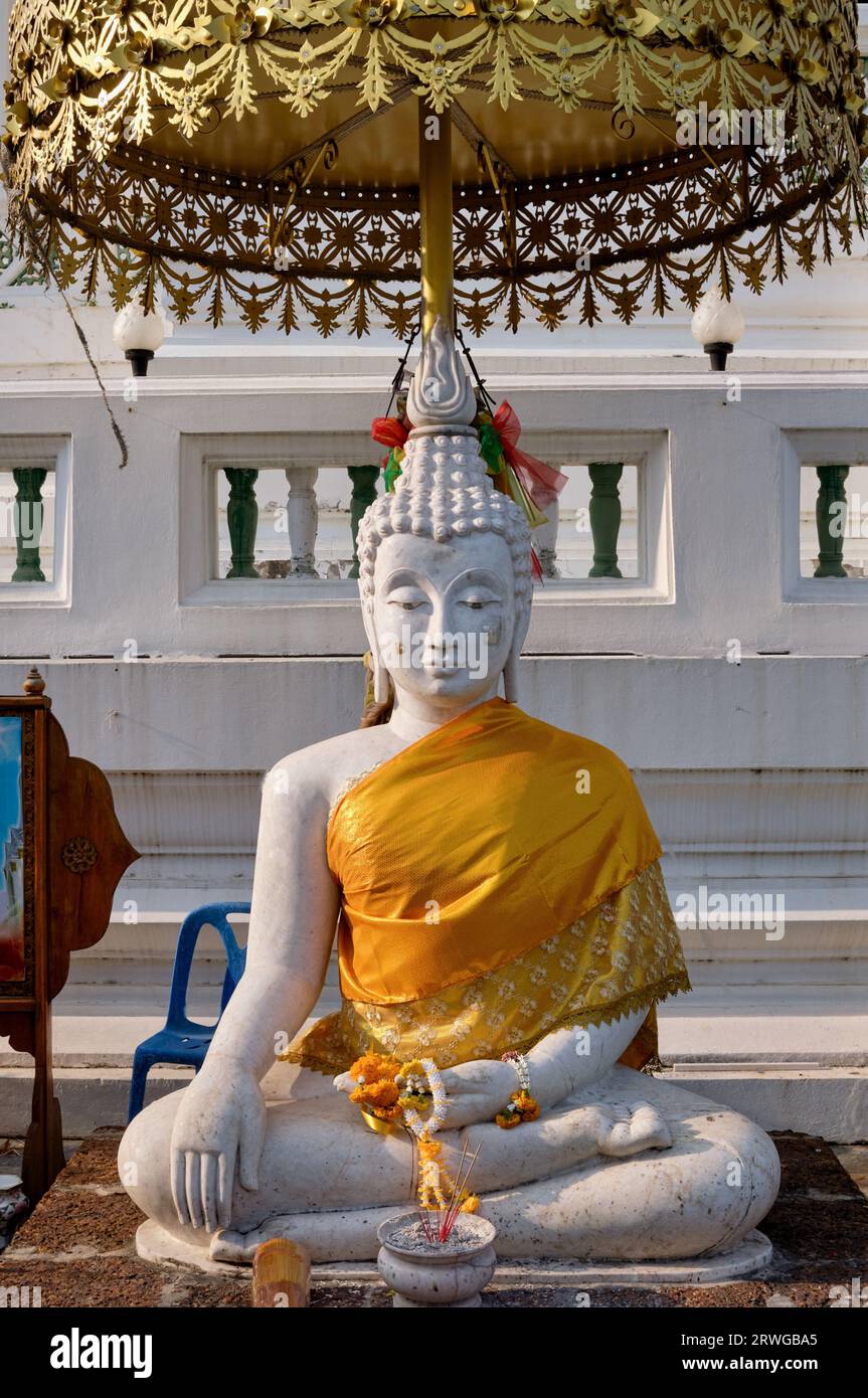 Une figure de Bouddha blanche assise dans le parc du Wat Pichaiyat, Thonburi, Bangkok, Thaïlande, couverte par un parapluie cérémoniel Banque D'Images