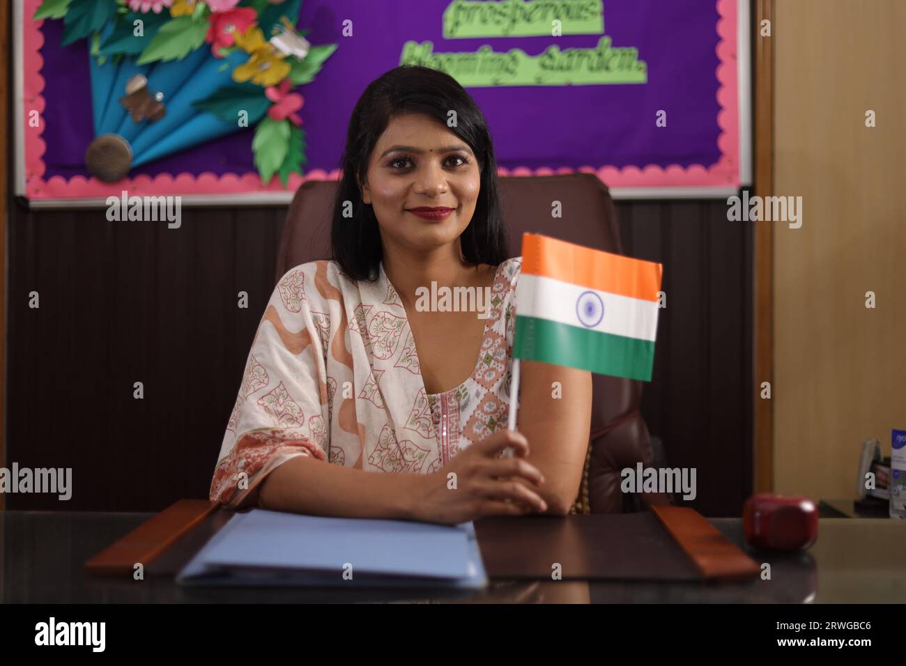 Fière directrice d'école présentant le drapeau indien assis en toute confiance dans son bureau. regarder dans la caméra Banque D'Images