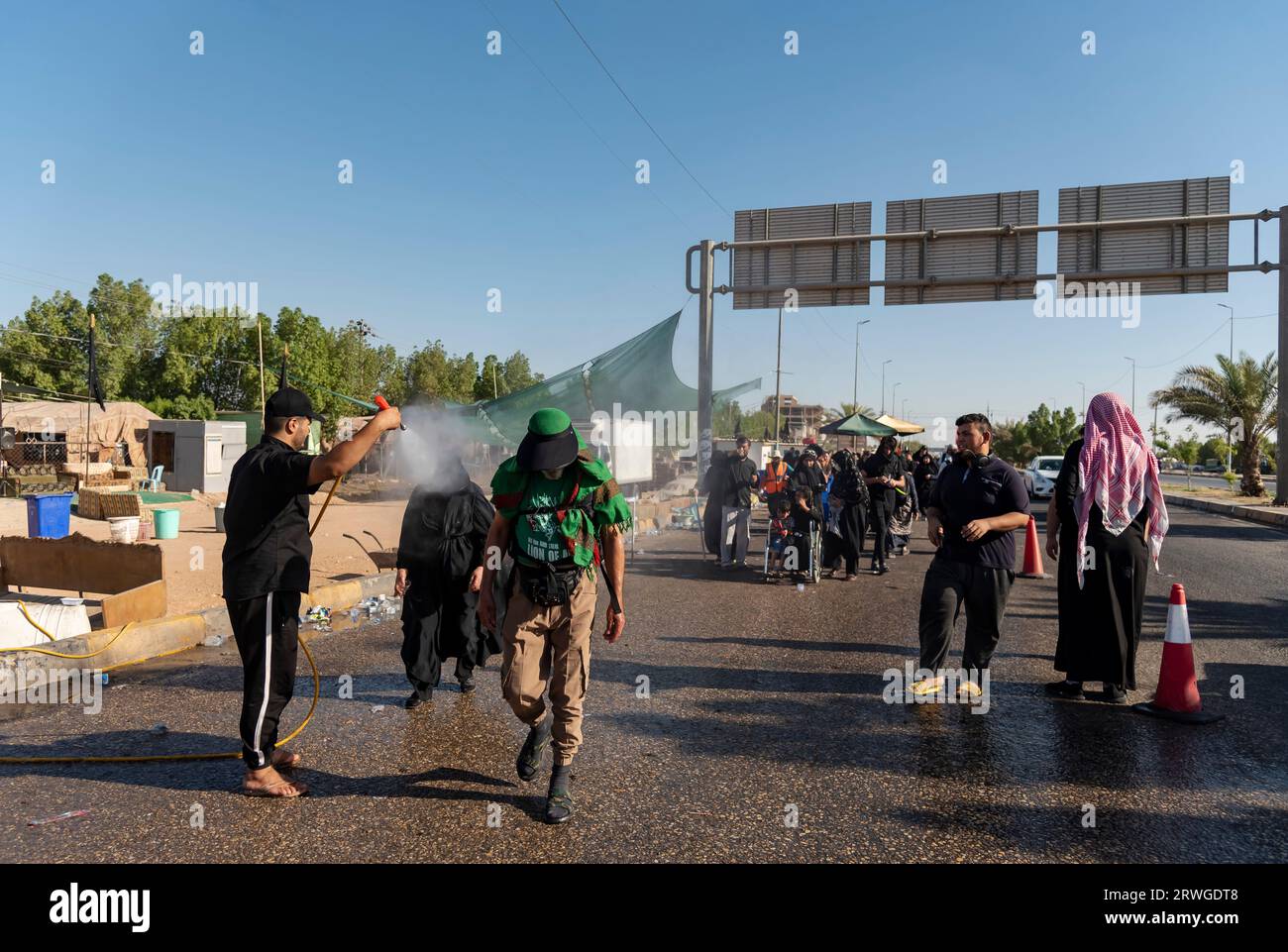 Un homme asperge d'eau les pèlerins musulmans chiites marchant de Najaf vers la ville sanctuaire de Karbala. Chaque année, des millions de musulmans chiites et certains d'autres confessions entreprennent un pèlerinage de 20 jours à pied depuis diverses villes d'Irak et d'Iran jusqu'à la ville sainte de Karbala. Ce pèlerinage est en souvenir de l'Imam Hussein, le petit-fils du Prophète Muhammad, mort dans une bataille en 680 AD. Le 40e jour de deuil de Hussein, connu sous le nom d'Arbaeen, les pèlerins convergent à Karbala pour rendre hommage à son sanctuaire. Sur le chemin, les bénévoles fournissent de la nourriture, de l'eau et un abri, et les villageois ouvrent leurs portes Banque D'Images