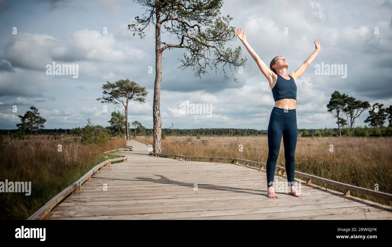 Athlète féminine levant les bras vers le ciel après l'exercice, debout sur une promenade. Banque D'Images