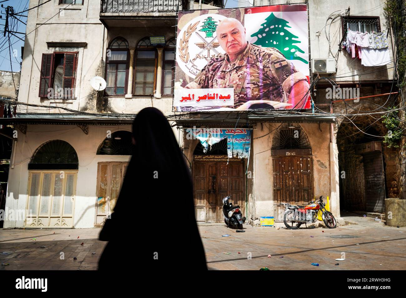 Femme voilée dans la ville de Tripoli, Liban. Sur le mur de la maison se trouve une affiche électorale d'un chef de l'armée. Banque D'Images