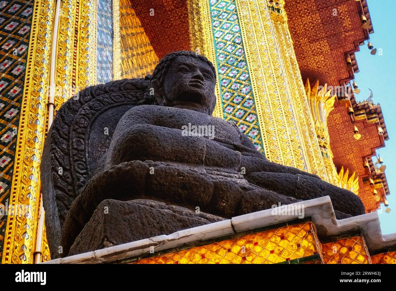 Une statue contemplative de Bouddha dans un temple. La statue noire, en repos sur un stand, est posée sur un fond énergique de dessins ornés dans gol Banque D'Images