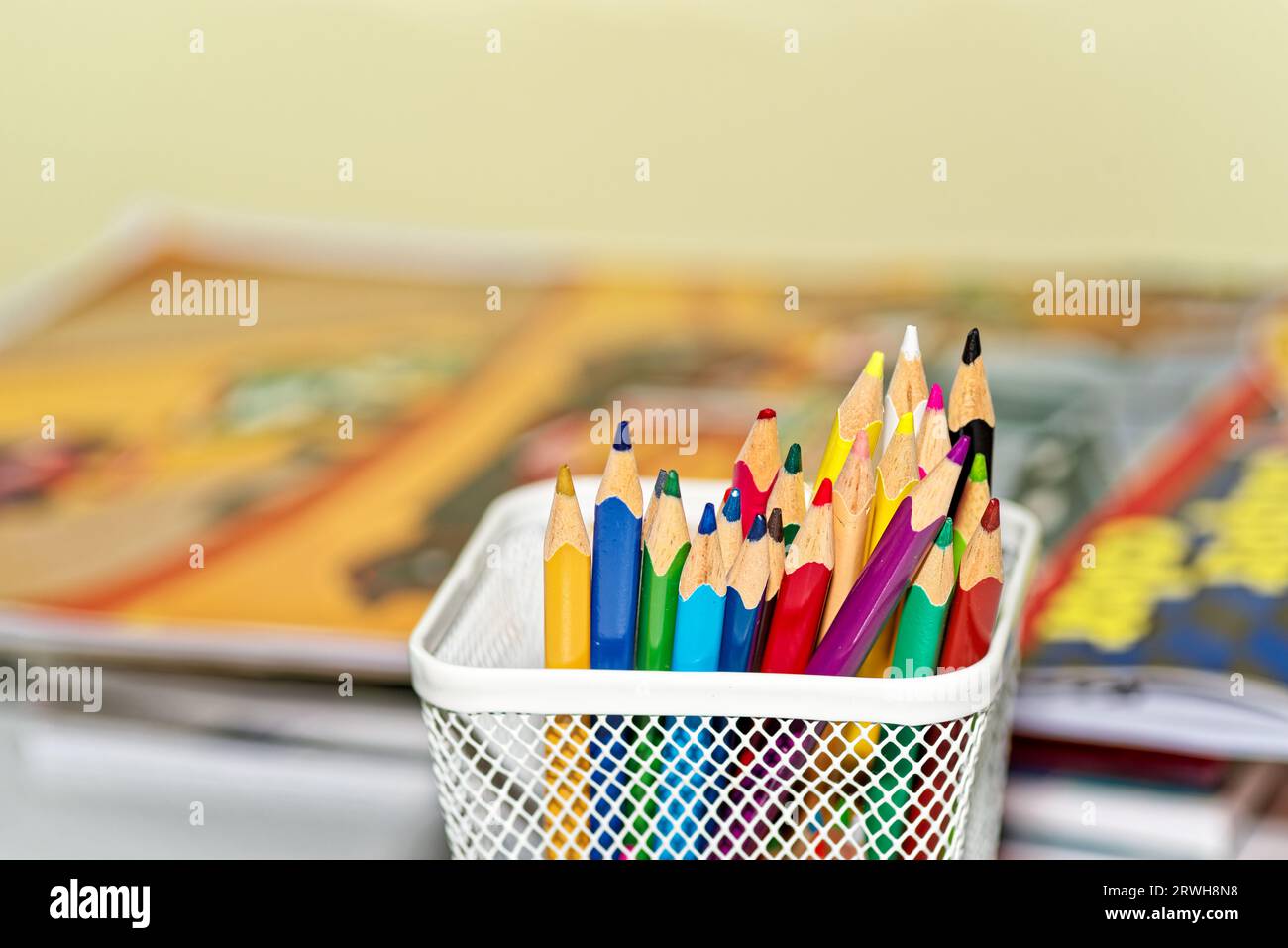 Crayons de couleur dans une boîte contre des livres défocalisés Banque D'Images