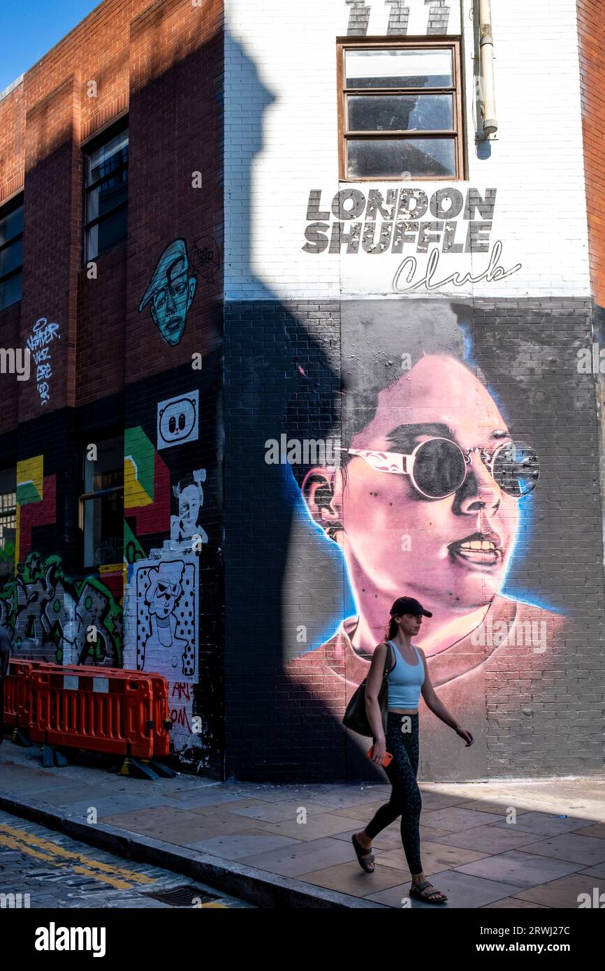 Une jeune femme passe devant Some Colourful Street Art, Shoreditch, Londres, Royaume-Uni. Banque D'Images