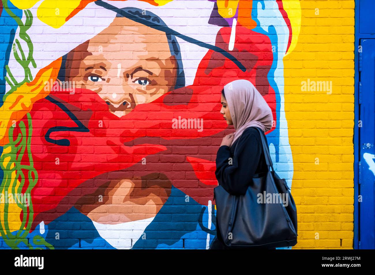 Une jeune femme passe devant Some Colourful Street Art, Shoreditch, Londres, Royaume-Uni. Banque D'Images