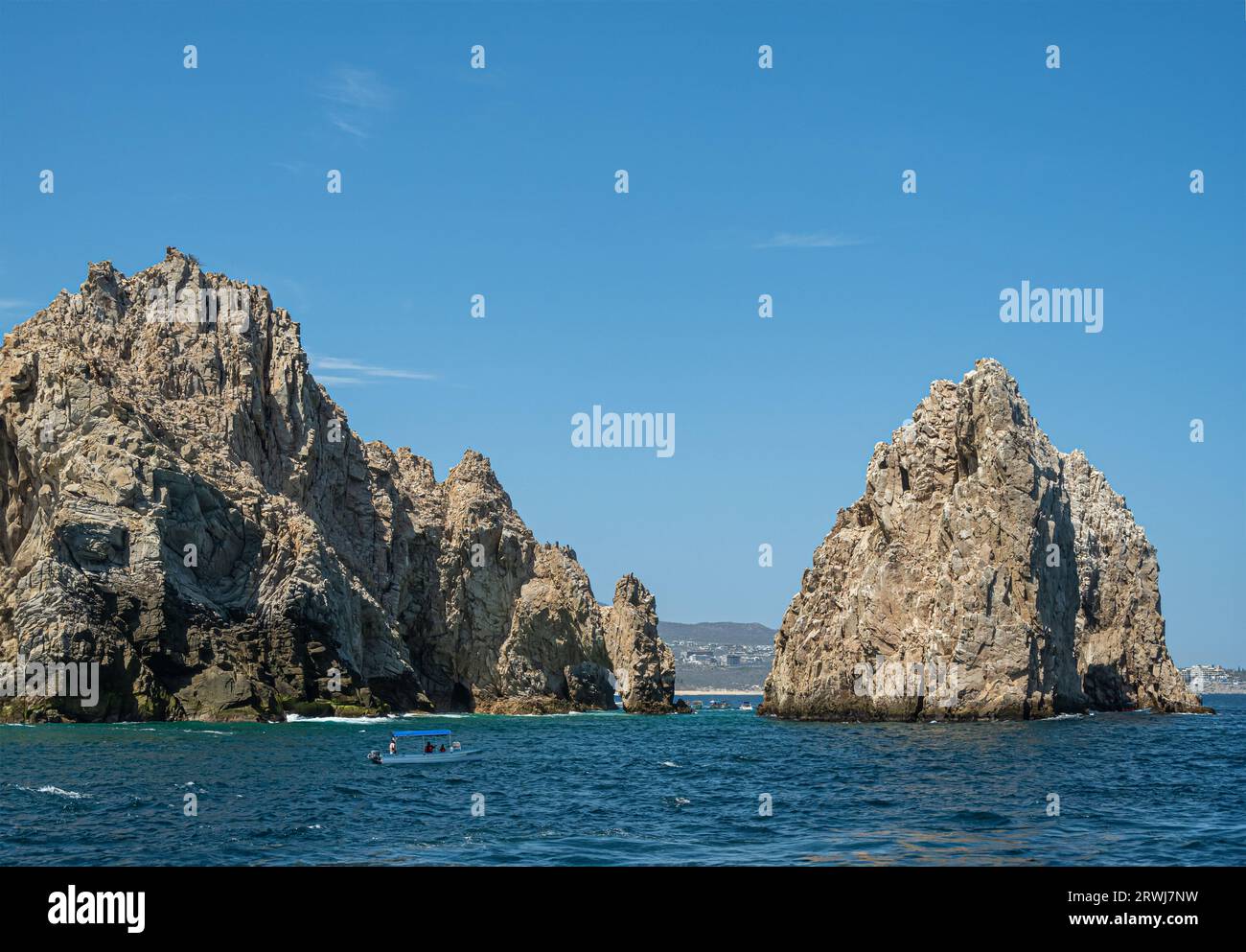 Mexique, Cabo San Lucas - 16 juillet 2023 : rochers rocheux comme la péninsule Reserva de lobos Marina se terminent dans l'eau bleue de l'océan avec paysage urbain à l'horizon. El Arco Banque D'Images